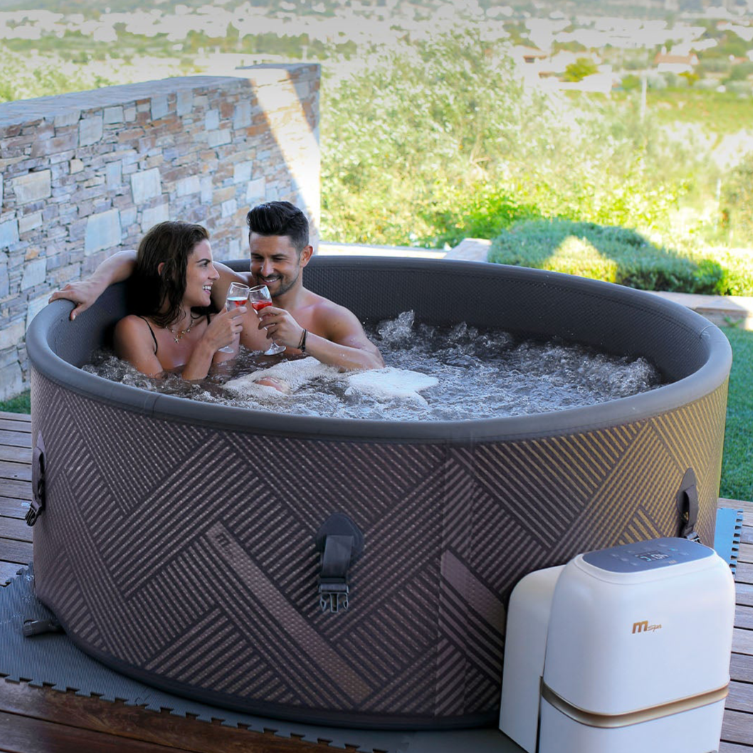 Round brown inflatable hot tub with chevron pattern exterior, two people relaxing inside on wooden deck outdoors. - Home Interior Shop - MSpa Mono Eco 4-6 Person Inflatable Hot Tub