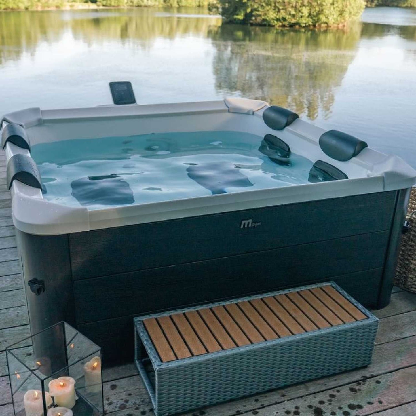Square grey MSpa Oslo portable hard frame hot tub with black headrests, filled with water, on wooden deck by a lake,. - Home Interior Shop - MSpa Oslo 4-6 Person Portable Hard Frame Hot Tub - Grey
