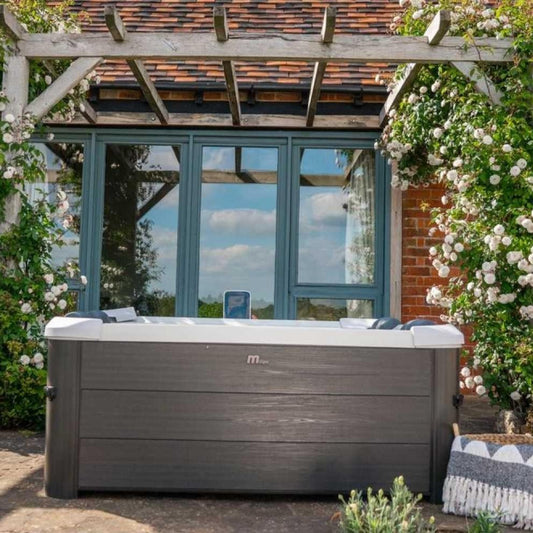 Portable grey hard frame hot tub with wood-textured paneling, set outdoors in front of glass doors surrounded by climbing. - Home Interior Shop - MSpa Oslo 4-6 Person Portable Hard Frame Hot Tub - Grey