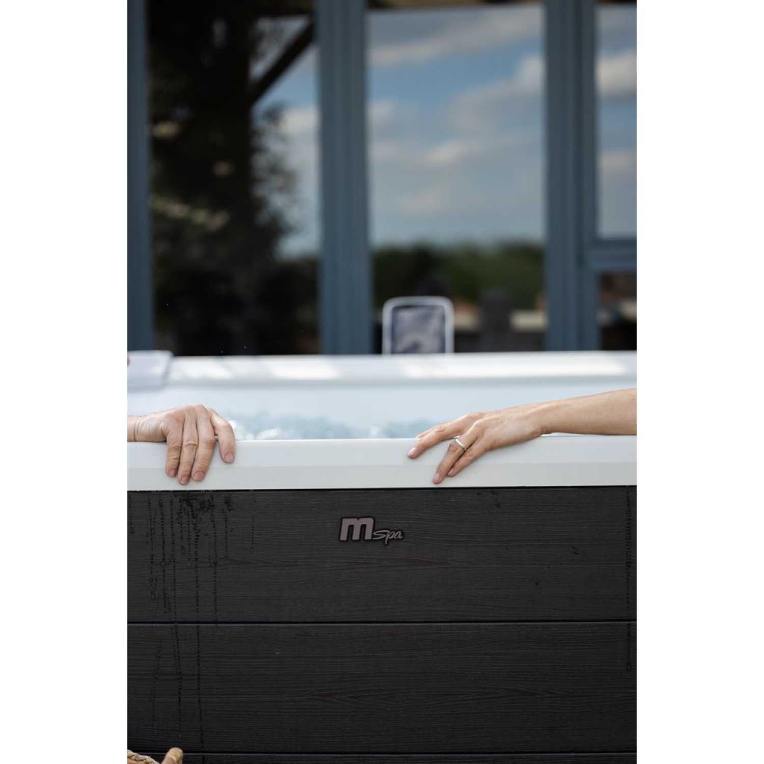 Grey square portable hard frame hot tub with two hands resting on opposite sides above bubbling water. - Home Interior Shop - MSpa Oslo Plus XL Portable Hard Frame Hot Tub - Grey