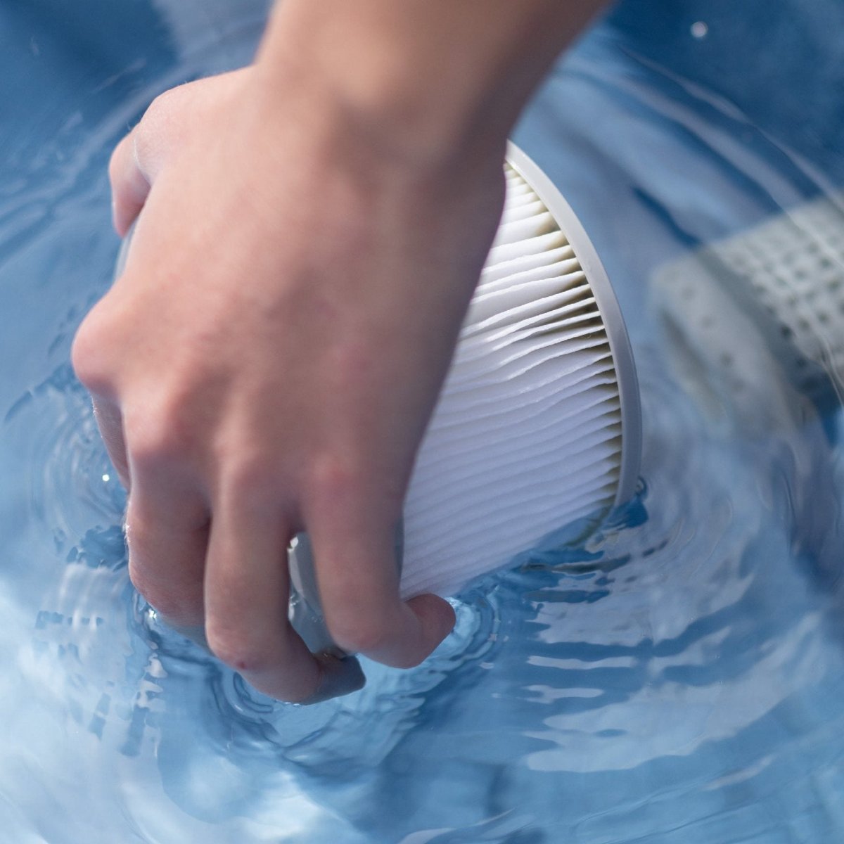 Hand holding a white pleated cylindrical filter cartridge submerged in blue water. - Home Interior Shop - MSpa Oslo & Tribeca LF90 Replacement Filter Cartridges (Set of 2) - Multi-Buy Discount